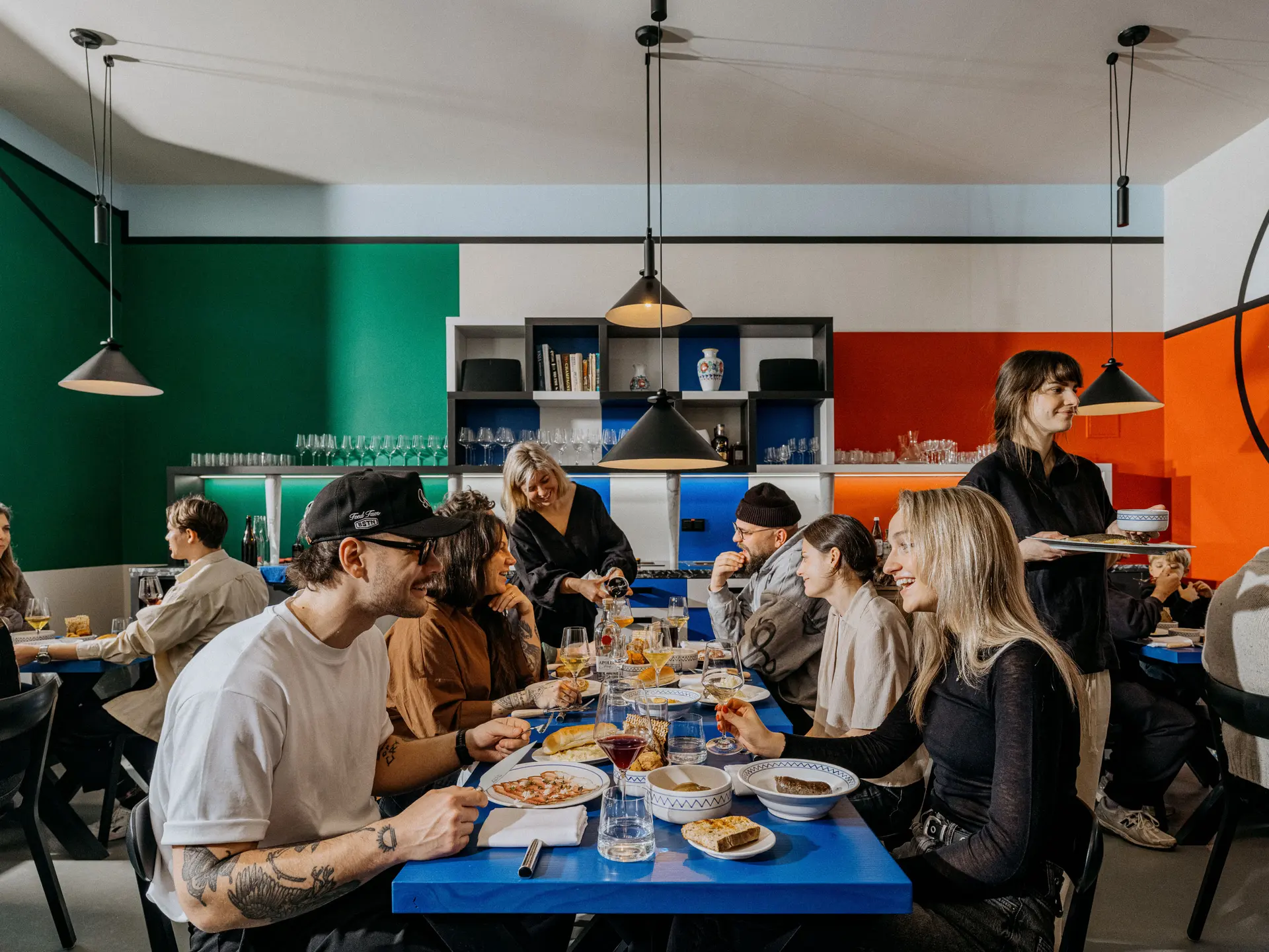 Hosté sedí u stolů v restauraci Skô a společně večeří.