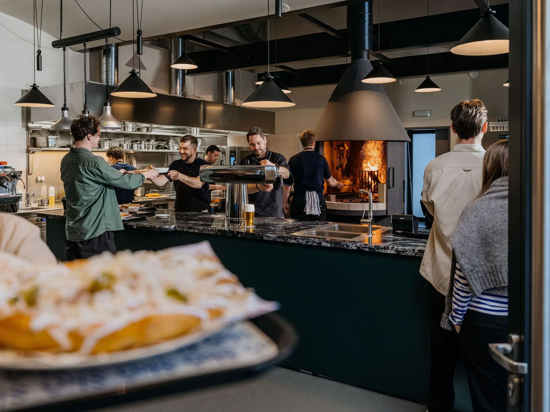 Pult v restauraci Skô s kuchaři při práci a otevřeným ohništěm v pozadí.